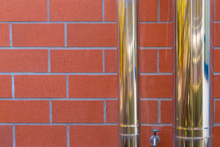 Two metallic shiny pipes in front of a red brick wallの写真素材