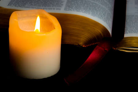 Old Bible with golden edge pages lighted by candlelight of a nearby candleの写真素材