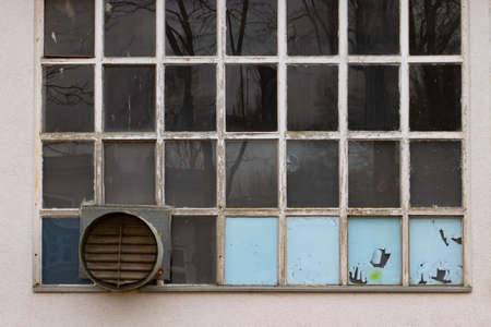 Old and broken industrial factory window with built in ventilation fan