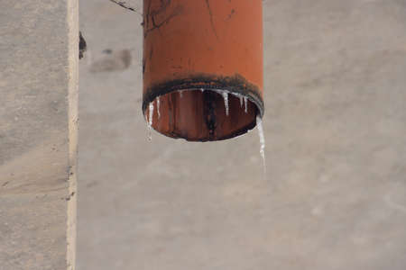 Melting icicles on a red plastic drainage pipe