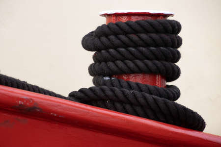 Black rope tied to a red metal mooring bollardの写真素材