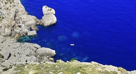 A white sail boat in a rocky bay on the Spanish island of Majorca in a wonderfully dark blue water.の写真素材