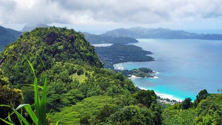 A Panoramic View of nature on the Seychelles with green forests, fresh plants, towering hills, white beaches, turquoise blue water under cloudy skyの写真素材