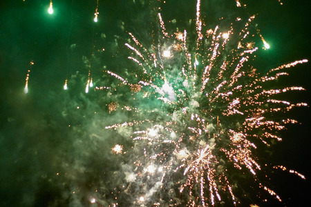 Fireworks rockets explode in the green illuminated night sky with lots of smoke and sparksの写真素材
