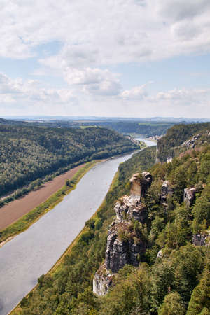 View from the Bastei viewpoint in the Saxon Switzerland hiking area over the Elbe valley with a beautiful sandstone rock formation in the foreground amidst green forestsの写真素材