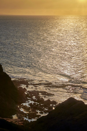 Sea coast in the evening light, upright format, gentle small waves in the sunset in front of the...