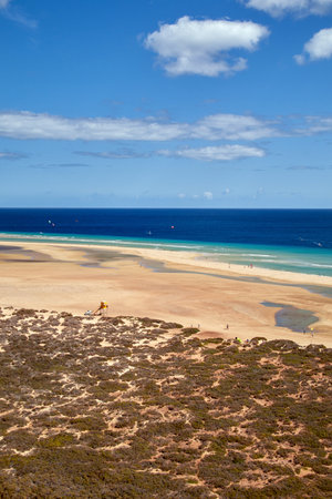 View over a wide beautiful bathing bay on the Canary Island Fuerteventura in the Atlantic Ocean, vertical photo, with beautiful summer weather and slightly cloudy blue skyの写真素材