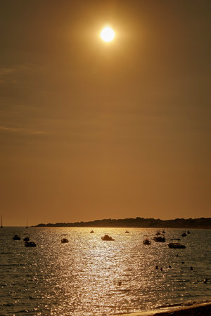 West coast of Corfu, bathing bay with small boats and people bathing in the sunset in the orange evening light sky, uprightの写真素材