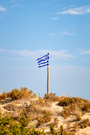 blue white Greek national flag waving in the wind on a sand duneの写真素材