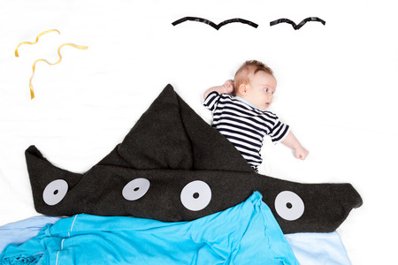 Small baby styled as sailor with ship made of blanketの写真素材