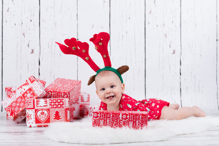 Baby as raindeer laying and smiling next to giftsの写真素材