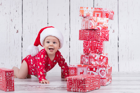 Little baby in red with cap crawling and smiling next to gift towerの写真素材