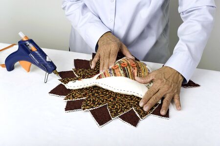 A woman pressing turkey body into place atop  feathers to create aThanksgiving  decoration.