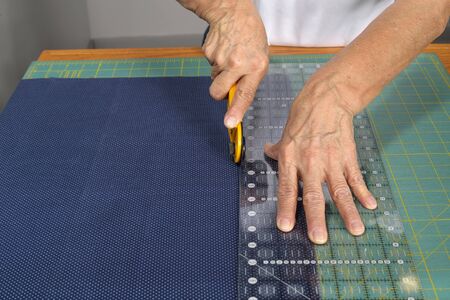A woman quilter cuts blue fabric with a rotary cutter for use in a new quilt.