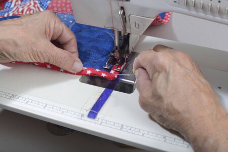 A quilter uses a stihletto to guide the fabric to complete a mitered corner on a quilt.