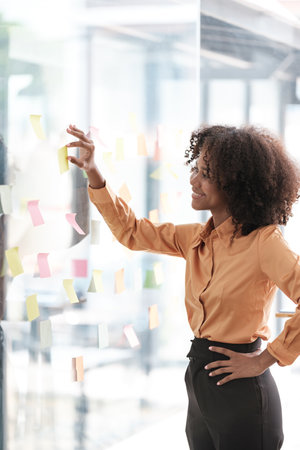 African American female employee write down on colorful sticky notes manage list, concentrated...