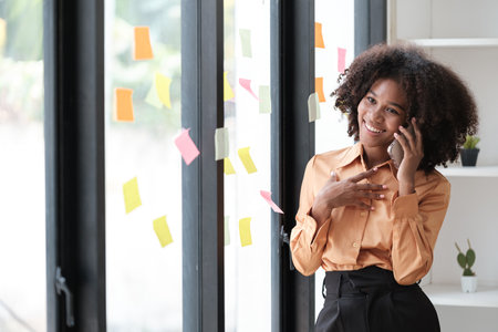 African American female employee write down on colorful sticky notes manage list, concentrated biracial woman work on startup brainstorm collaborate plan on stickers on glass wallの写真素材
