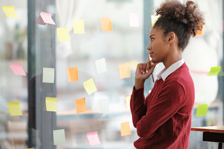 African American female employee write down on colorful sticky notes manage list, concentrated...