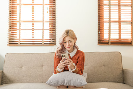 Young asian woman using a smart phone sitting on the sofa in the room. Order some online shopping.の写真素材