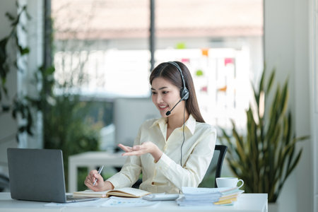 Portrait of happy smiling female customer support phone operator at workplace. Asianの写真素材