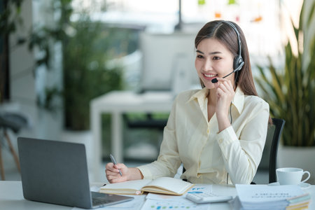 Portrait of happy smiling female customer support phone operator at workplace. Asianの写真素材