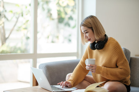 Beautiful asian woman online learning with laptop in living room.の写真素材