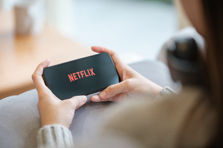 CHIANG MAI, THAILAND - Jun 23, 2023 : A woman hold apple iPhone 14 pro with Netflix entertainment platform in living room at home.のeditorial素材