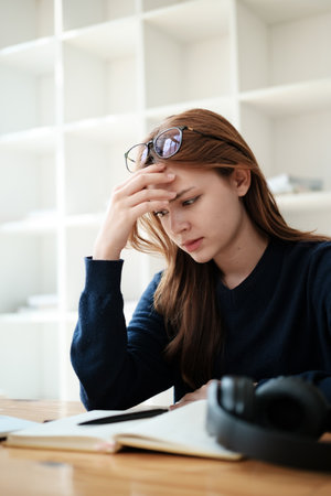 A beautiful caucasian female student is studying remotely. She is sitting at a table at home with a laptop and a notepad and concentrated is watching a video conference, Thinking.の写真素材