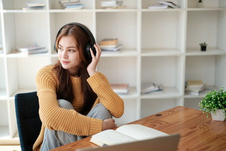 A beautiful caucasian female student is studying remotely. She is sitting at a table at home with a...