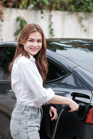 Young woman traveling by electric car having stop at charging station standing plugging charger close-up.の写真素材