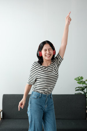 Attractive and happy young Asian woman in casual clothes wearing headphones, relaxes listening to music in her home office.の写真素材