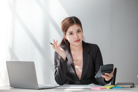Asian Business woman using calculator and laptop for doing math finance on an office desk, tax, report, accounting, statistics, and analytical research conceptの写真素材