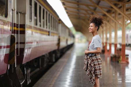 Young Asian African woman traveler with backpack in the railway train station, traveler girl walking stand sit waiting take a picture on railway platform train station. High quality photoの写真素材