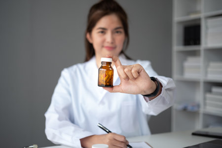 Young beautiful asian woman doctor holding pills bottle writing on document at clinic.の写真素材