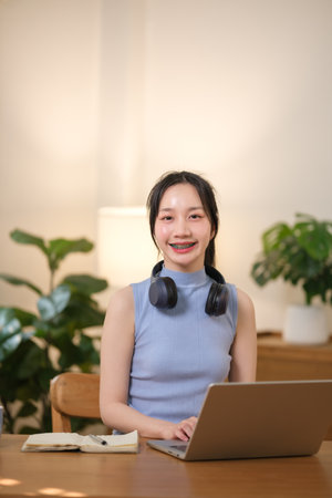 Young attractive happy Asian female student sitting in the living room smiling and looking at the...