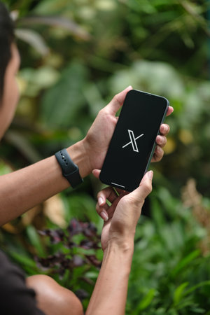 CHIANG MAI, THAILAND - Jul. 28,2023 : a Man holding an iPhone 14 Pro Max with X or Twitter application on the screen. Instagram is a popular online social networking service.のeditorial素材