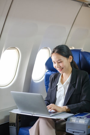 A woman is sitting in an airplane and using a laptop