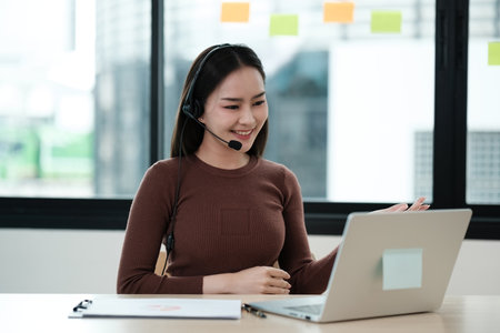 A woman wearing a headset is smiling at a laptopの写真素材