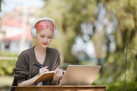 Young woman with a laptop and notes studying in the park for education in nature to relax and learn...