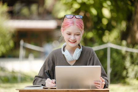 Young woman with a laptop and notes studying in the park for education in nature to relax and learn online.の写真素材