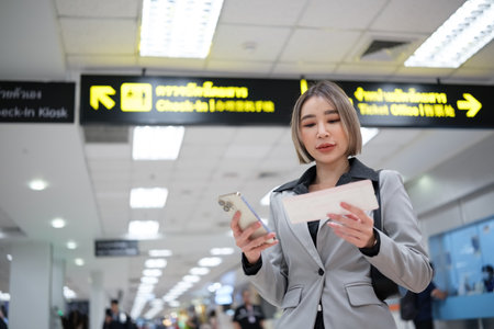 A woman is looking at her phone while reading a ticketの写真素材