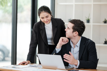 A woman and a man are sitting at a desk with a laptop in front of themの写真素材