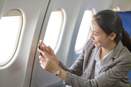 A woman is sitting in an airplane and taking a picture of the windowの写真素材