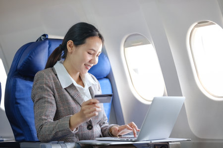 A woman is sitting in an airplane seat, using a laptop to pay for her ticket