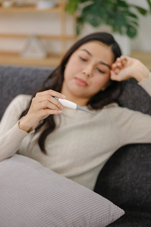 A woman is holding a thermometer and looking at it