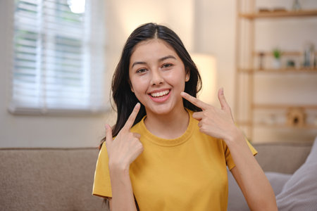 A woman in a yellow shirt is smiling and pointing at her teethの写真素材