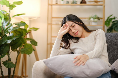 A woman is sitting on a couch with a pillow on her lapの写真素材