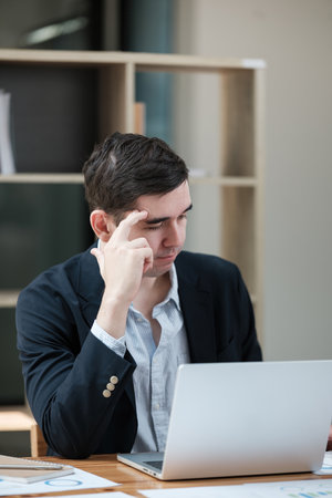 A man is sitting at a desk with a laptop in front of himの写真素材