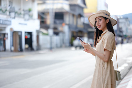 A woman in a hat is standing on a street holding a cell phoneの写真素材