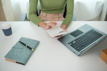A woman is sitting at a desk with a laptop and a calculatorの写真素材